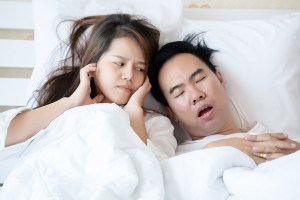 Couple in bed with man snoring and woman covering ears
